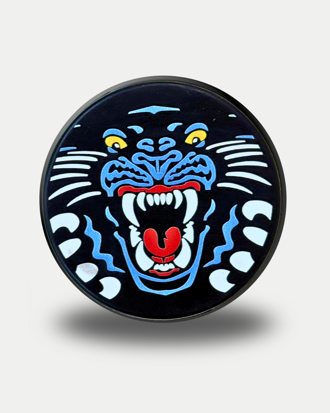 The Panthersland Nottingham Panthers 25-26 Big Crest Puck features a round design with a stylized roaring black panther head, blue, white, yellow, and red details on a dark background, open mouth displaying sharp teeth and a red tongue.