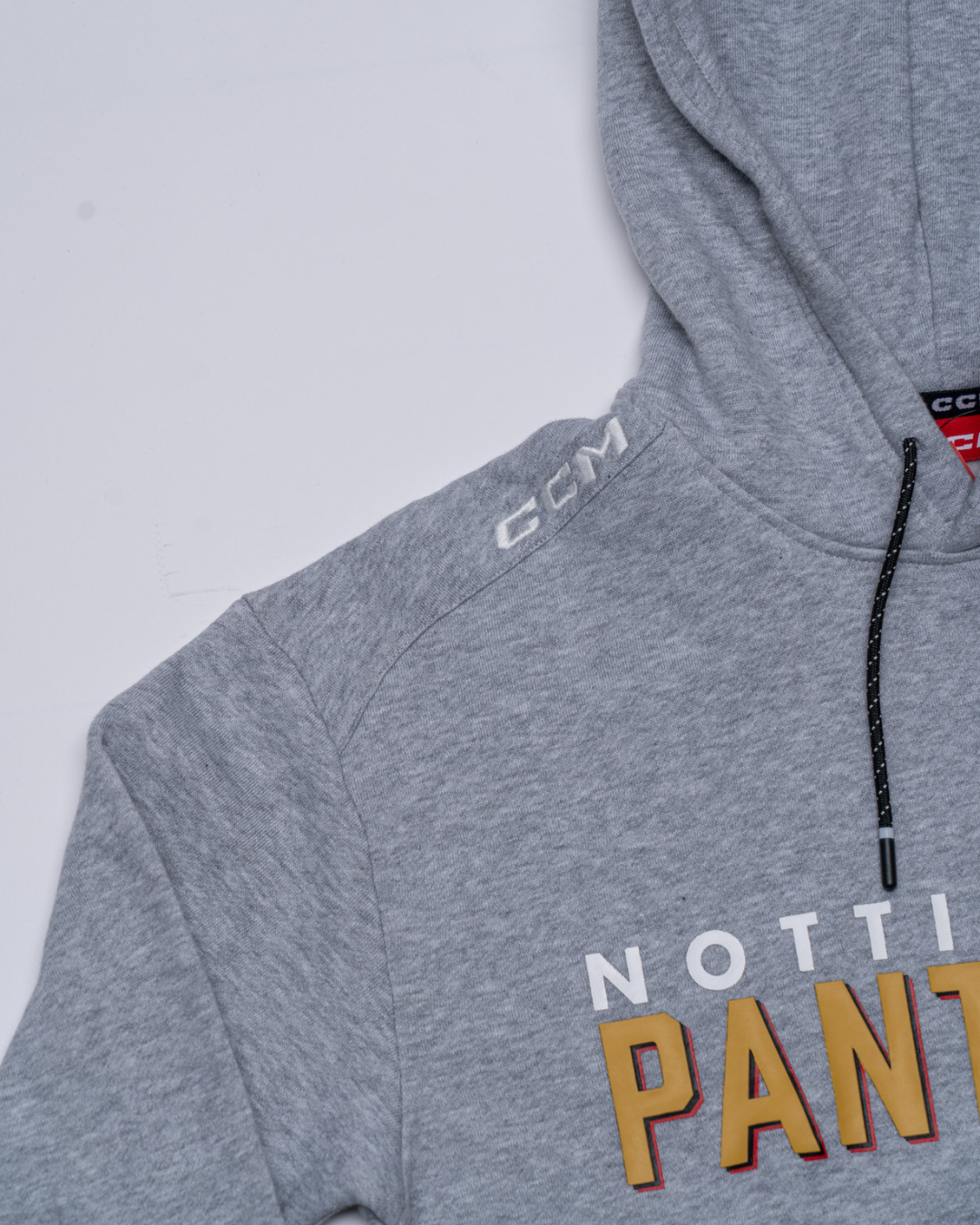 The Nottingham Panthers 25-26 CCM Grey Team Text Hoodie by Panthersland features "NOTT PANT" in white and gold on the chest, a hood with black drawstrings, and a white stitched CCM logo on the shoulder.