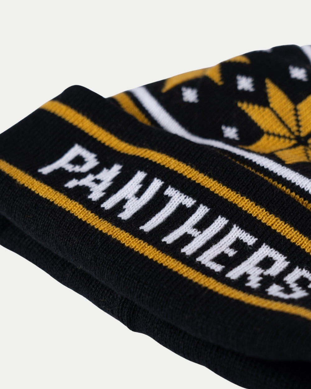 A close-up of the Nottingham Panthers Gold Snowflake Pom Knit, a black beanie with yellow and white stripes, bold “PANTHERS” lettering, and a partial yellow snowflake pattern above the text.
