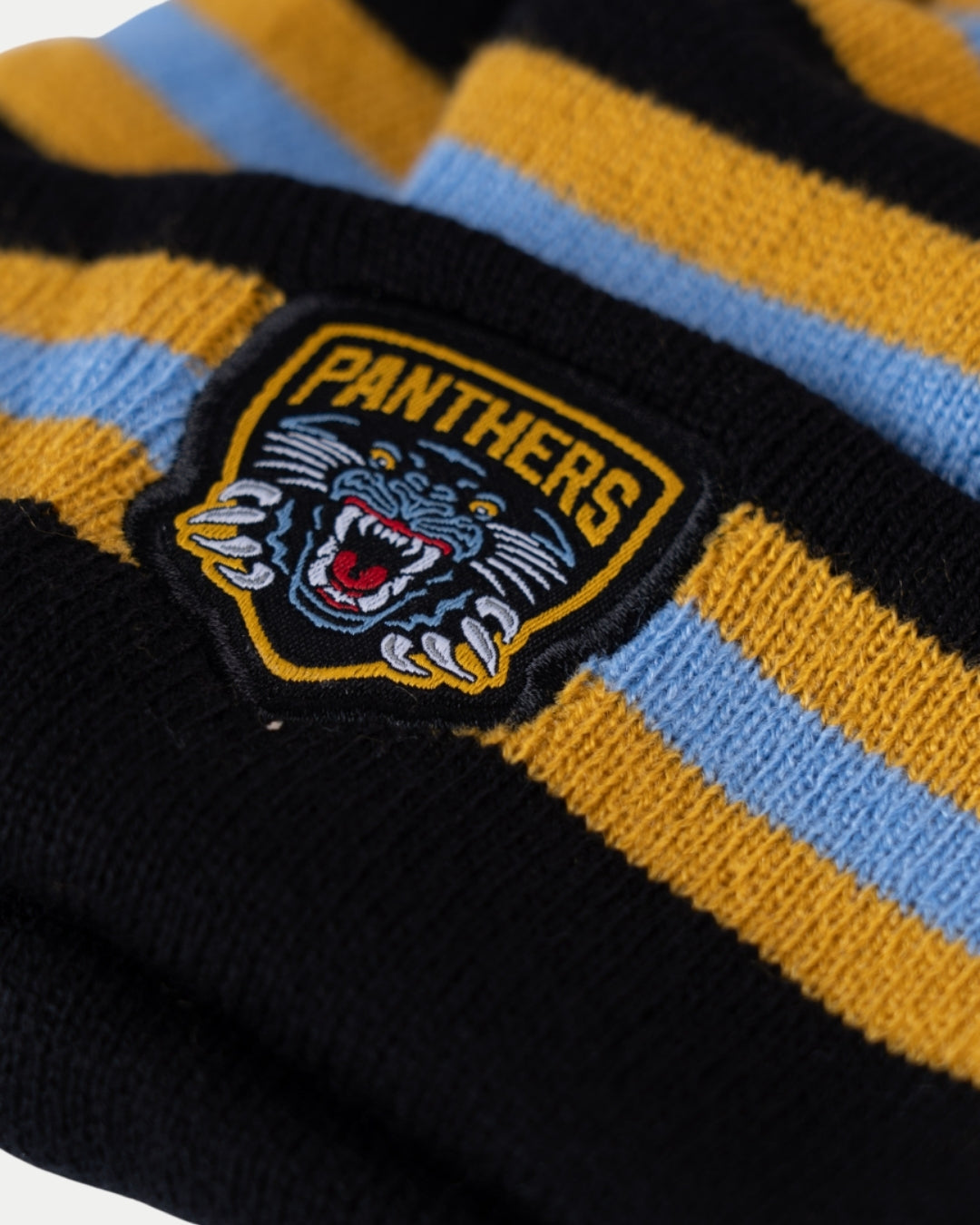 Close-up of the Nottingham Panthers 24-25 Blue Stripe Pom Knit by Nottingham Panthers, showing black, yellow, and blue stripes plus a patch with a roaring panther and bold PANTHERS text.