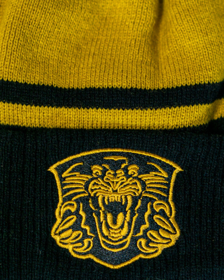 A close-up of the Panthersland Nottingham Panthers 25-26 Gold Stripe Pom Knit, featuring a yellow and black pattern with a gold pom and an embroidered roaring tiger face—an essential winter hat for fans.