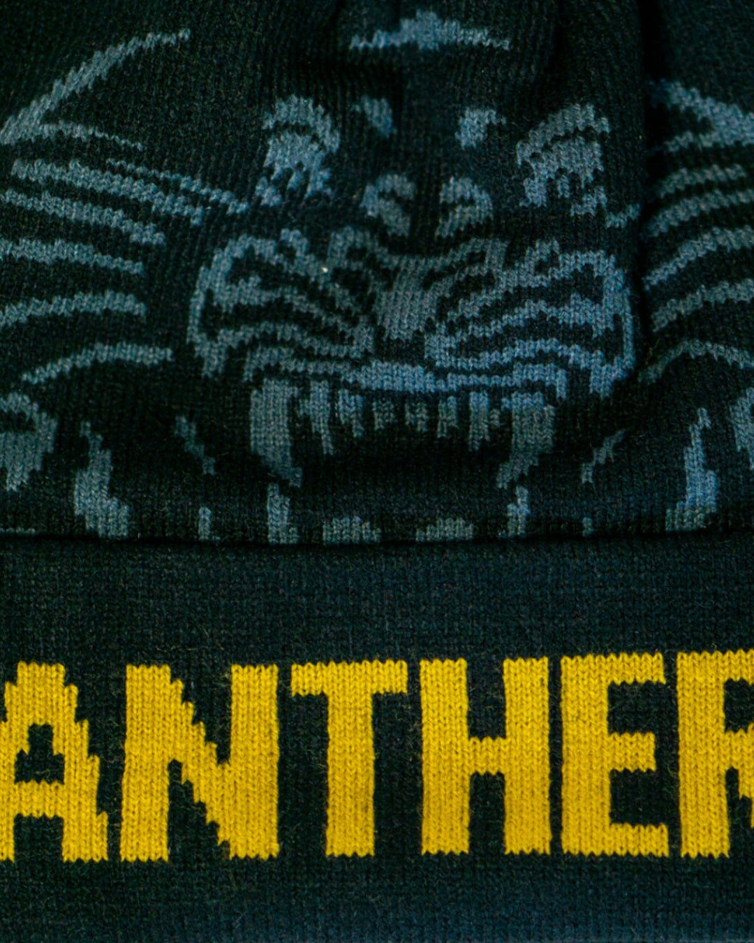 Close-up of the Panthersland Nottingham Panthers 25-26 Charcoal Crest Pom Knit beanie, showcasing a stylized panther face above bold yellow PANTHER text on a charcoal knit fabric.