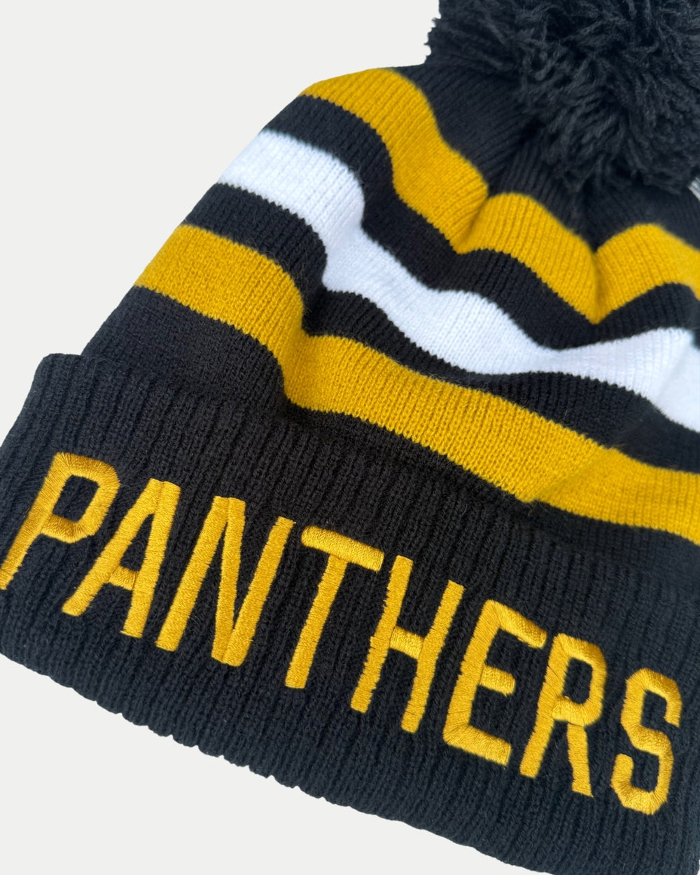 Stay warm in the Panthersland Nottingham Panthers 25-26 White Stripe Pom Knit, a striped winter beanie with black, gold, and white stripes, a fluffy black pom-pom, and “PANTHERS” boldly knitted in gold across the brim.