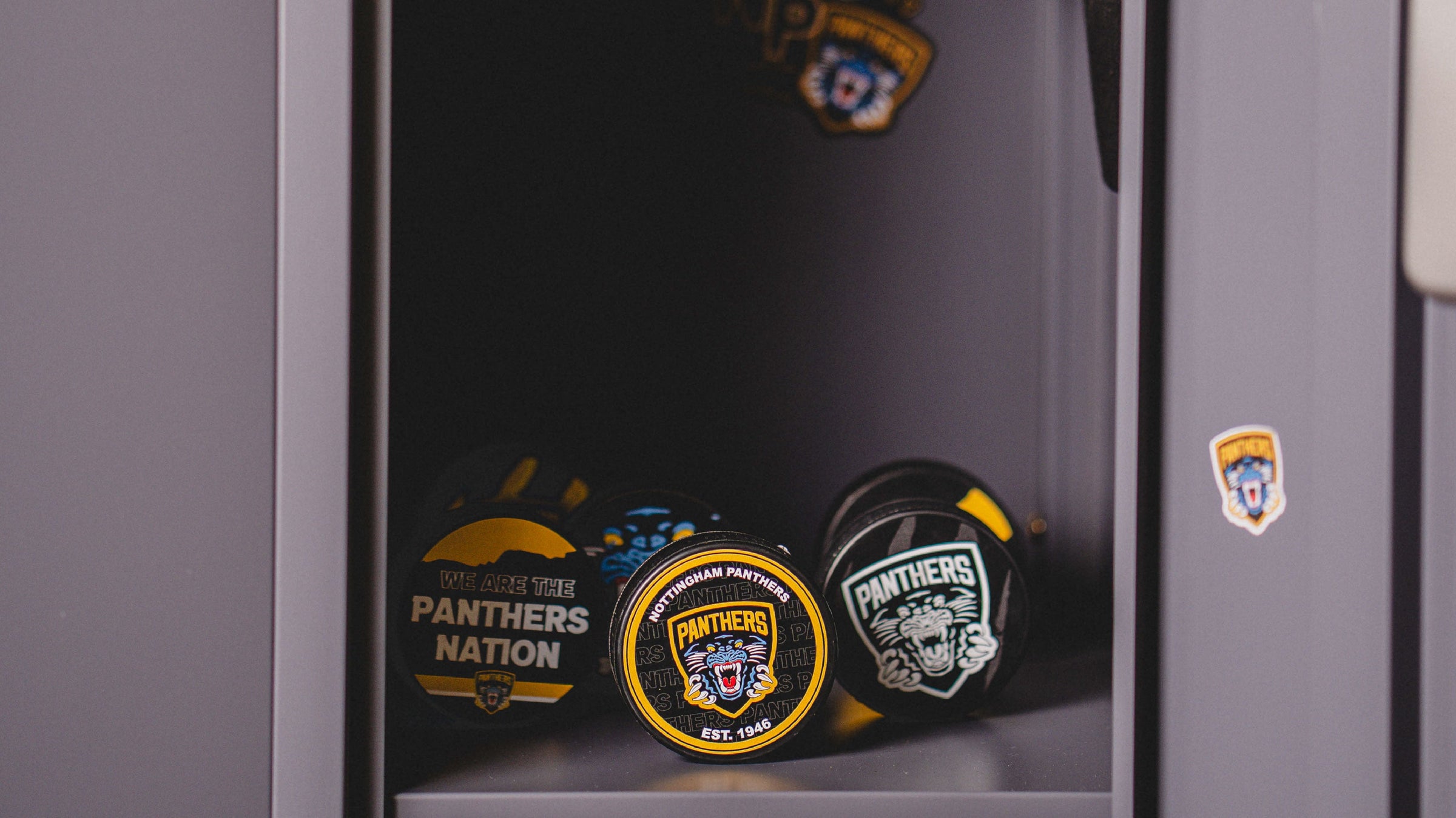 Three hockey pucks with Nottingham Panthers logos sit inside a gray locker, along with team stickers inside and on the locker door.