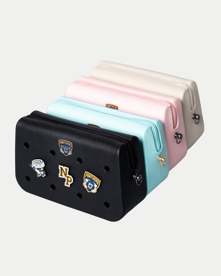 Four rectangular Nottingham Panthers Croc Charm Bags by Panthersland in black, light blue, pink, and beige are lined up. The black bag features decorative pins including a drum, NP letters, and two patch-style charms.
