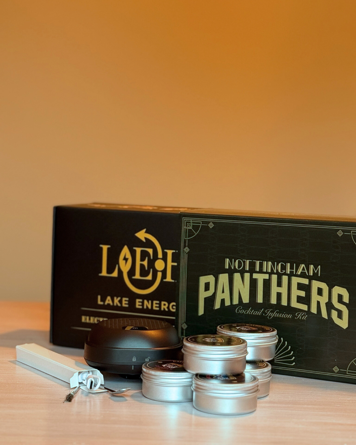 A Panthersland Nottingham Panthers Whiskey Smoker Kit, small metal tins, a black container, and a Lake Energy box are displayed on light wood with a warm orange background.