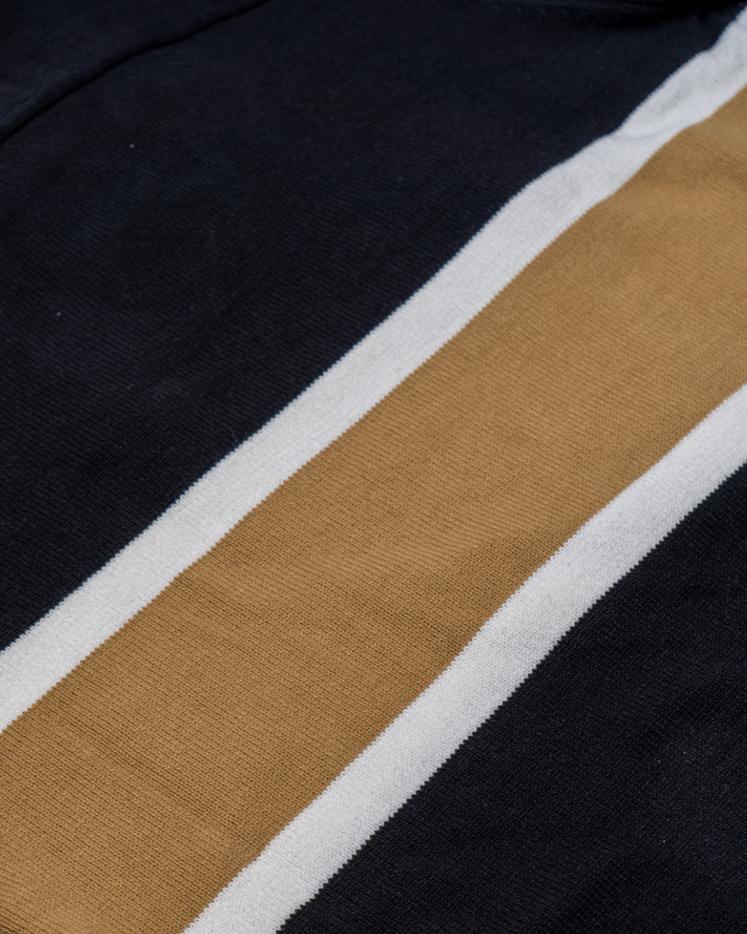 A close-up of the Nottingham Panthers 25-26 CCM Gold Heritage Sweater by Panthersland shows two white stripes flanking a single tan stripe on a black background.