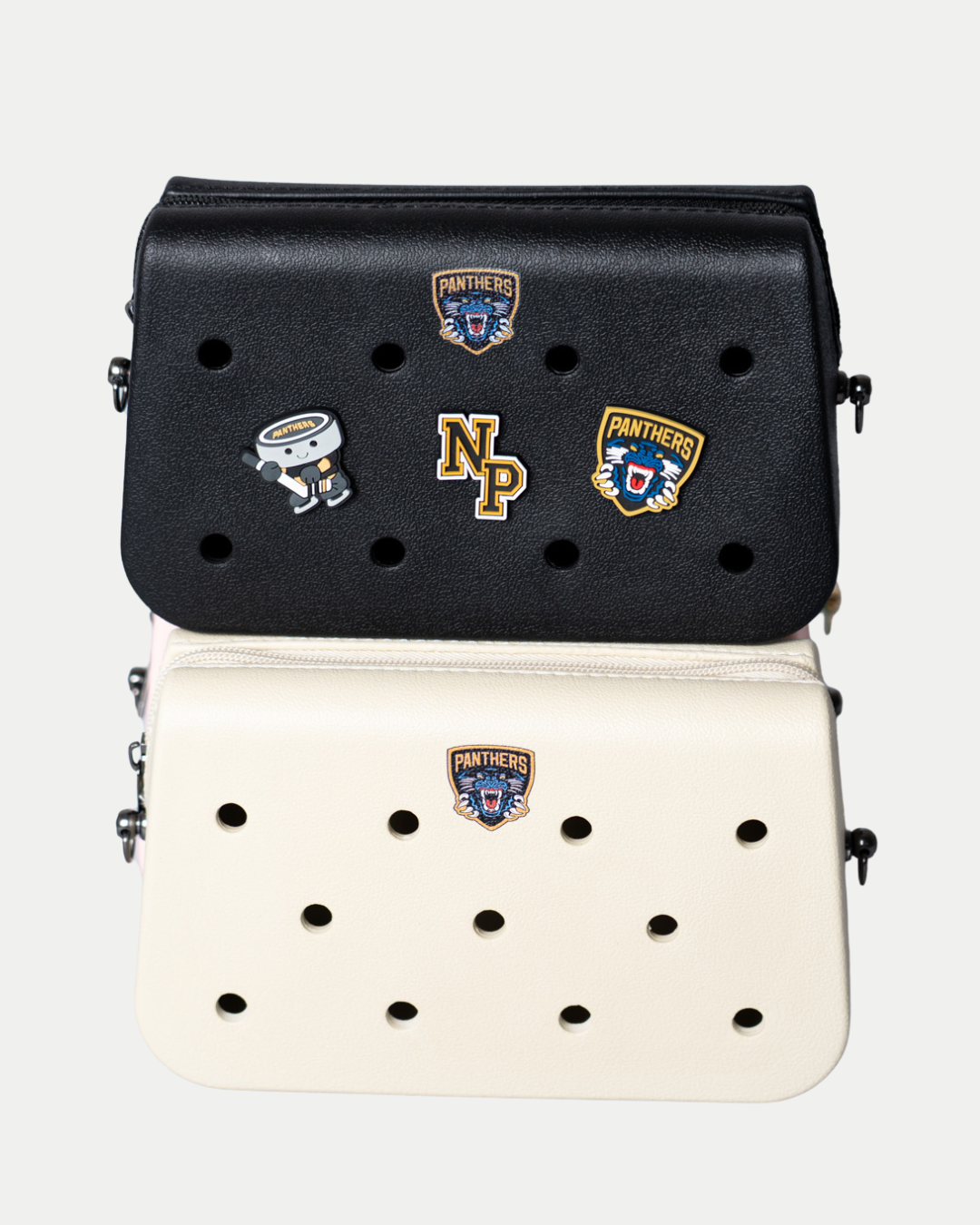 Two rectangular Nottingham Panthers Croc Charm Bags from Panthersland, one black and one white, are stacked on a plain white background. Both feature perforations, decorative pins with the logo, robot, and emblems reading “Panthers” and “NP.”.