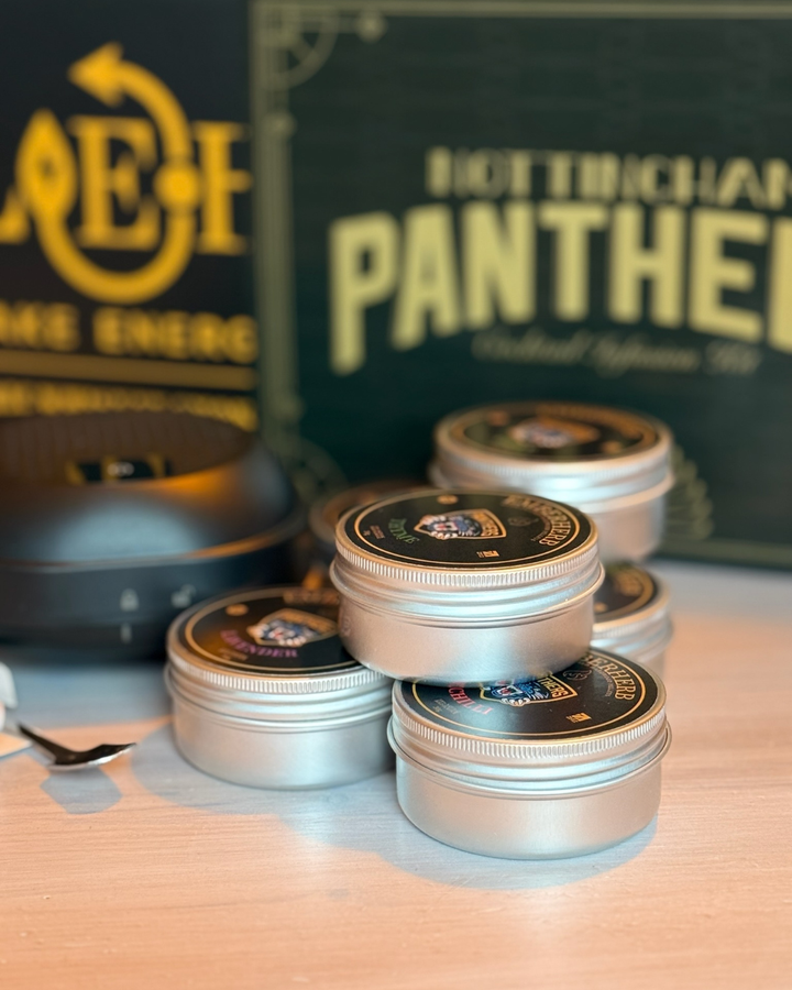 A stack of small silver tins with black lids and logos sits on a light wood surface. Nottingham Panthers and C4E branding are in the background—ideal for crafting drinks with the Panthersland Nottingham Panthers Whiskey Smoker Kit.