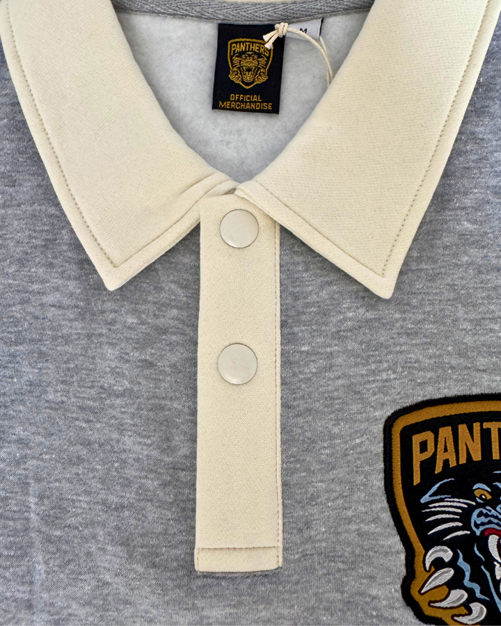 Check out the Panthersland 26-27 Grey Crest Sweater—a close-up look reveals a classic rugby-style design in grey with white trim, finished with two white buttons, an interior collar tag featuring “Panthers,” and a partial Panthers crest patch on the front. Perfect game day apparel for true fans.