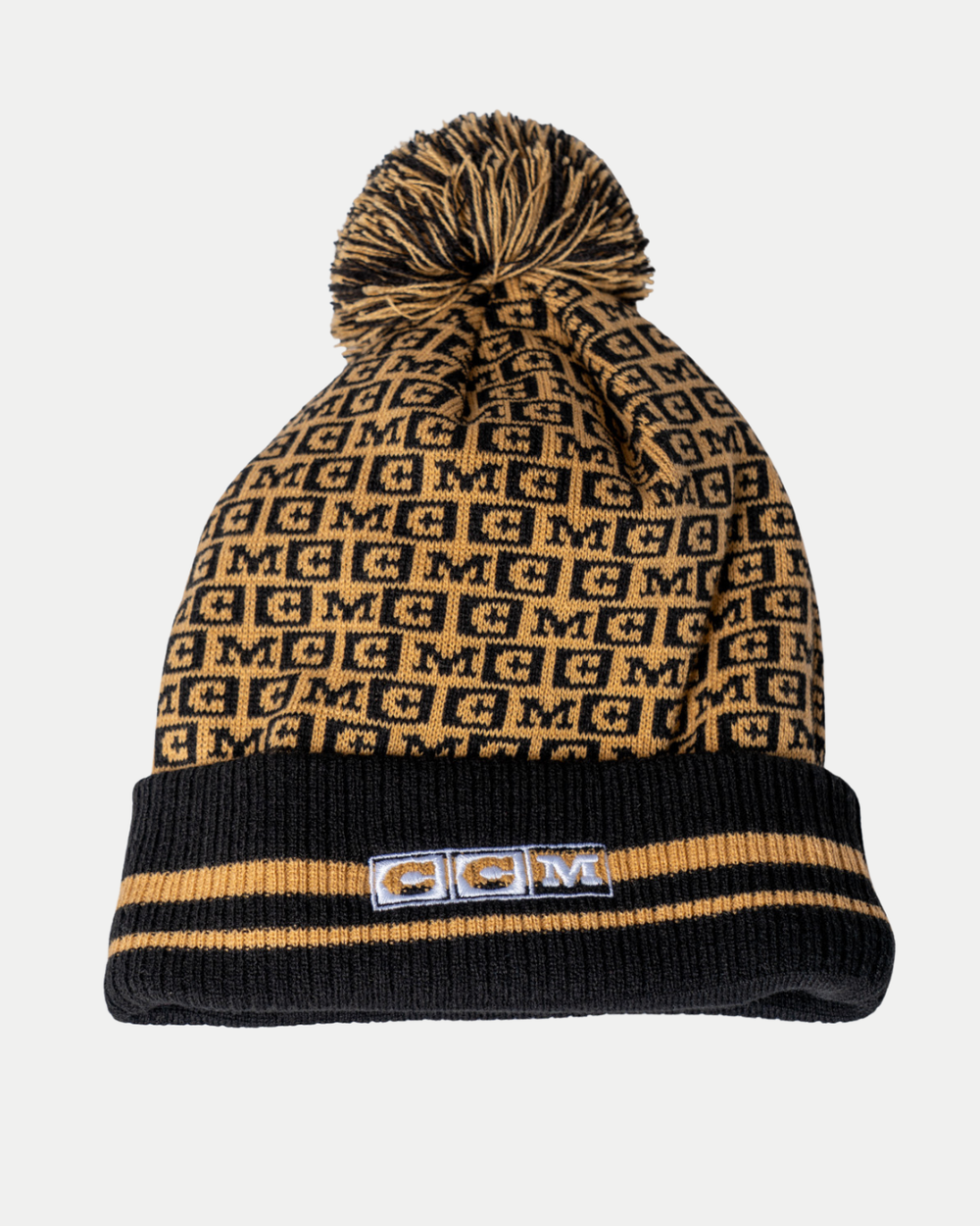 The Panthersland Nottingham Panthers 25-26 CCM Black Crest Pom Knit features a black and tan knit with repeated M letters, a pom-pom, two tan stripes on the rim, and an embroidered MCM logo patch on the front.