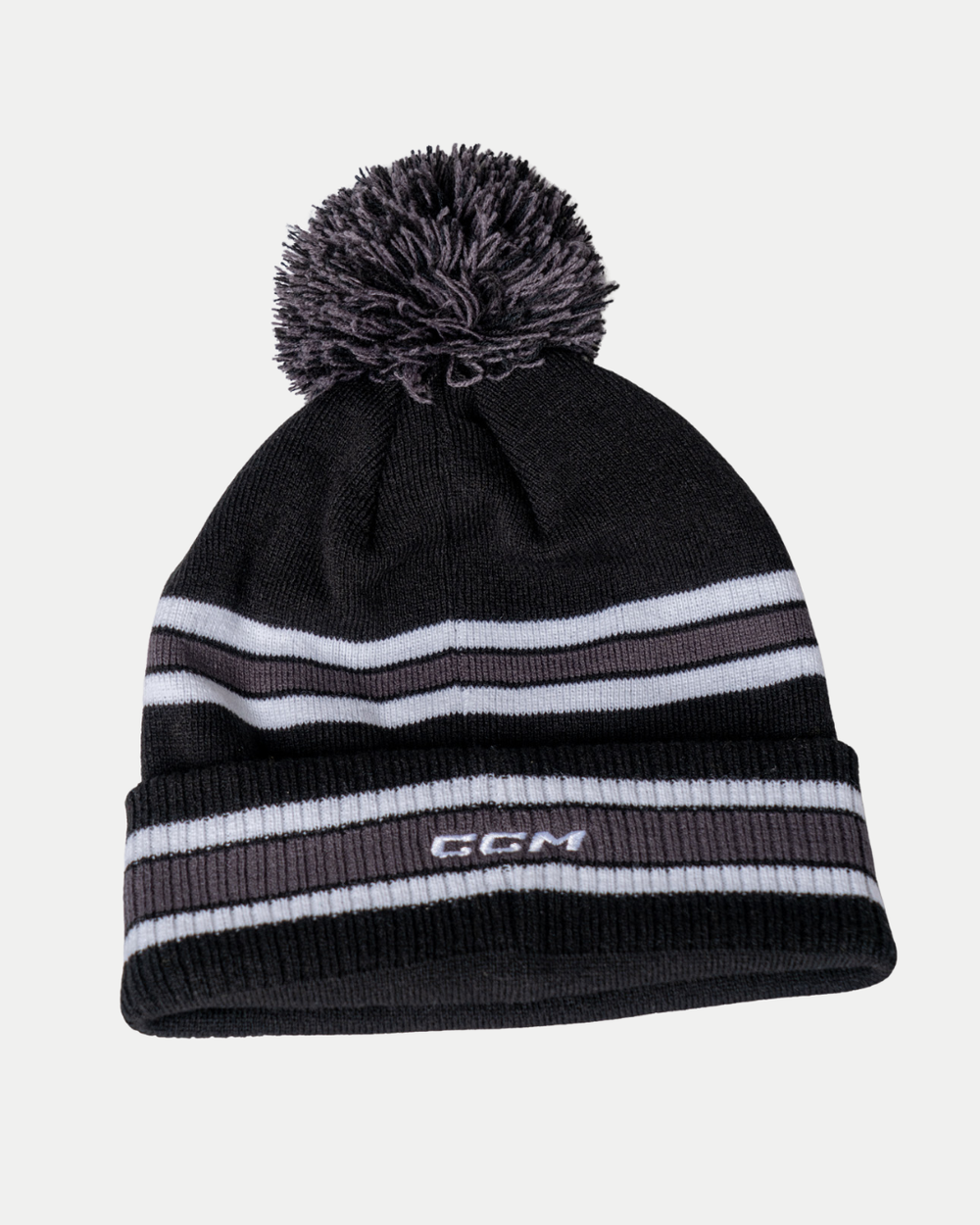The Nottingham Panthers 25-26 CCM White Stripe Pom Knit by Panthersland is a black beanie with gray and white horizontal stripes, a gray and black pom-pom, and white CCM embroidery on the front.