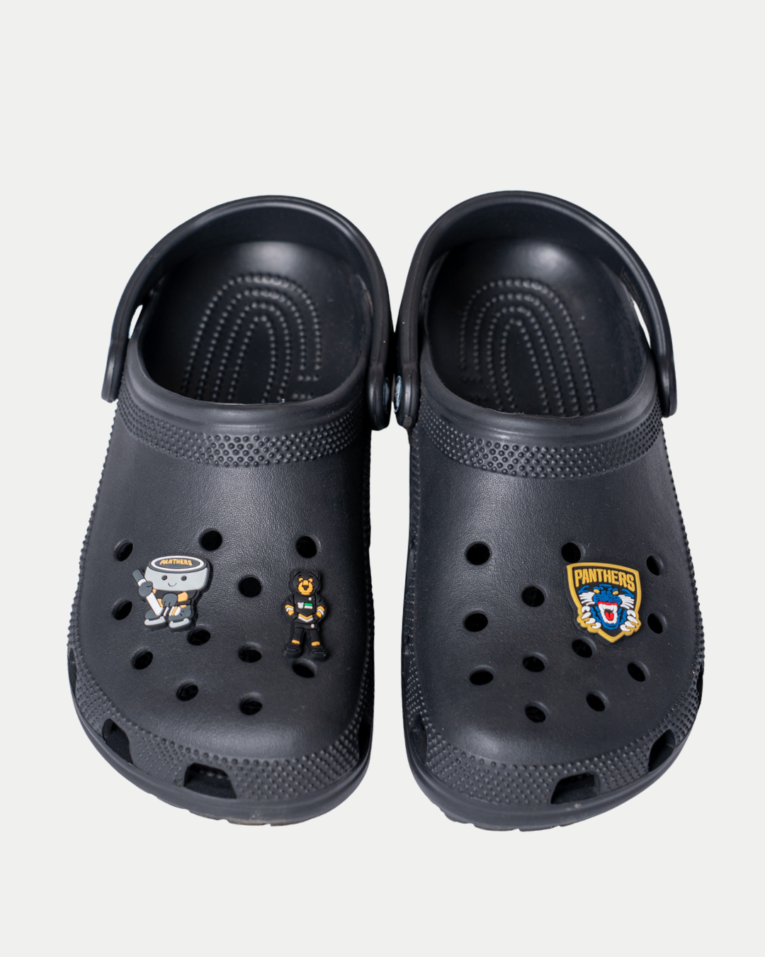 A pair of black clogs featuring two Panthersland Nottingham Panthers Logo Croc Charms attached to the shoe holes for a hockey-themed look.