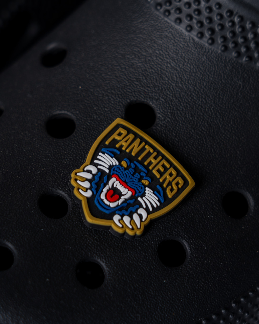 The Nottingham Panthers Logo Croc Charm by Panthersland features a snarling blue panther, yellow "PANTHERS" text, and pawed shield—an ideal accessory for any Nottingham Panthers fan.