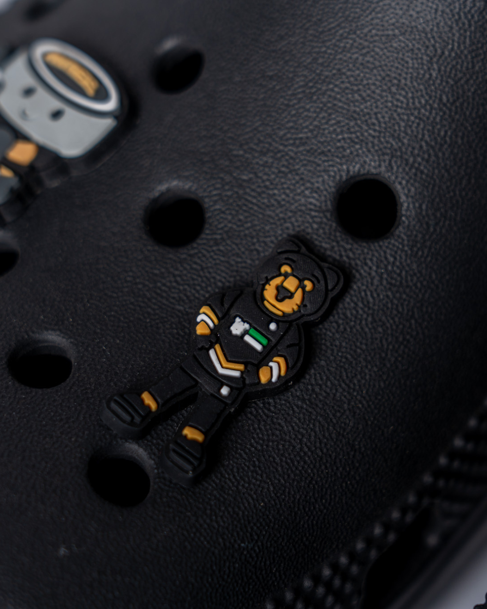 A black Crocs shoe features the Panthersland Paws Croc Charm—a Nottingham Panthers mascot bear in a black outfit with yellow, green, and white details—attached above the shoe’s circular ventilation holes.