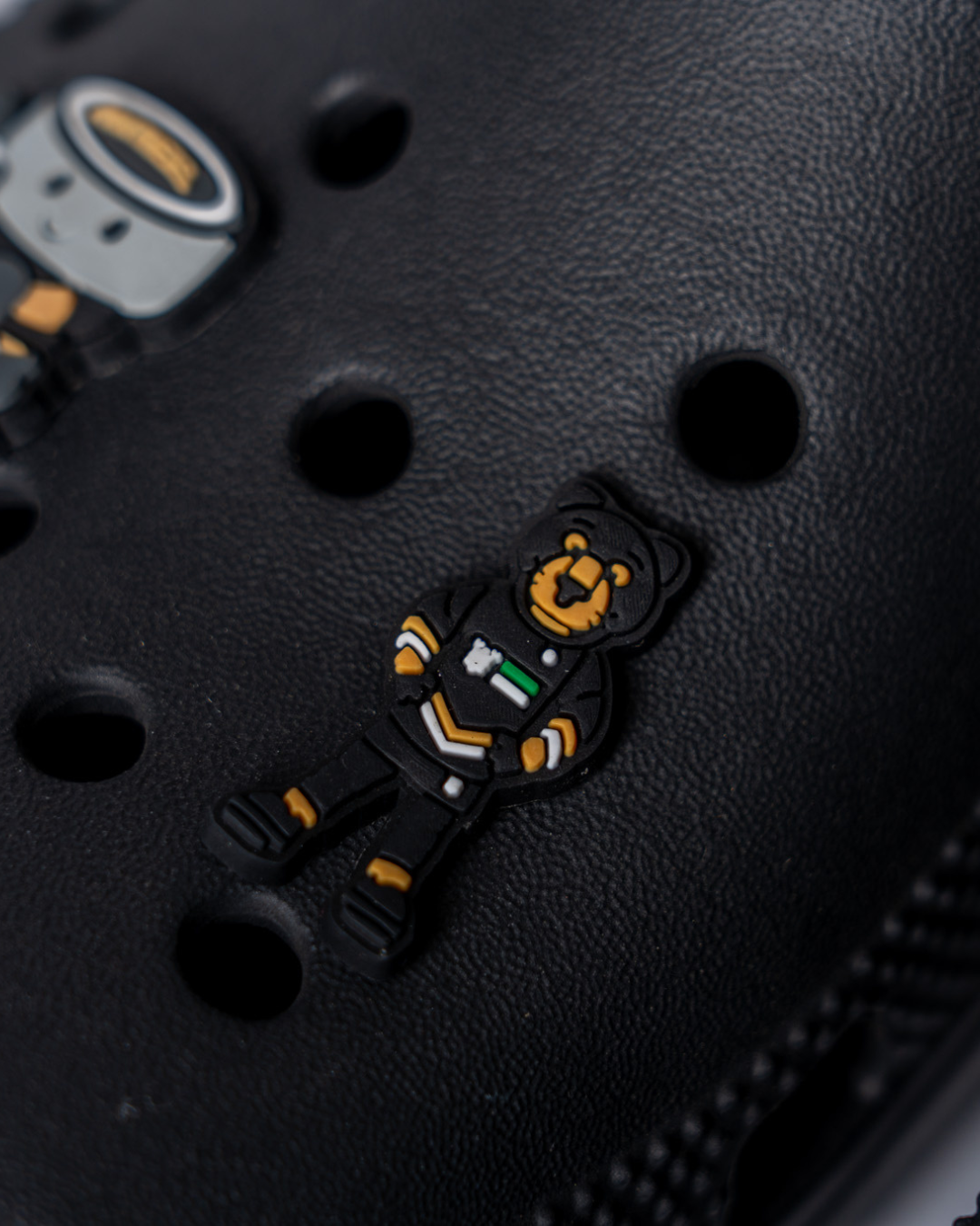 A black Crocs shoe features the Panthersland Paws Croc Charm—a Nottingham Panthers mascot bear in a black outfit with yellow, green, and white details—attached above the shoe’s circular ventilation holes.