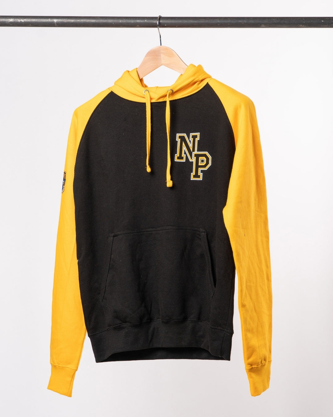 The Nottingham Panthers NP Logo Black/Gold Hoodie, featuring yellow sleeves, a front pocket, and NP initials in yellow on the left chest, hangs on a wooden hanger against a white background.