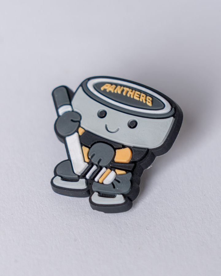The Nottingham Panthers 25-26 Puck Croc Charm by Panthersland features a smiling cartoon puck character with a white hockey stick and "PANTHERS" on top, displaying team spirit in black, gray, and yellow on a light gray base.