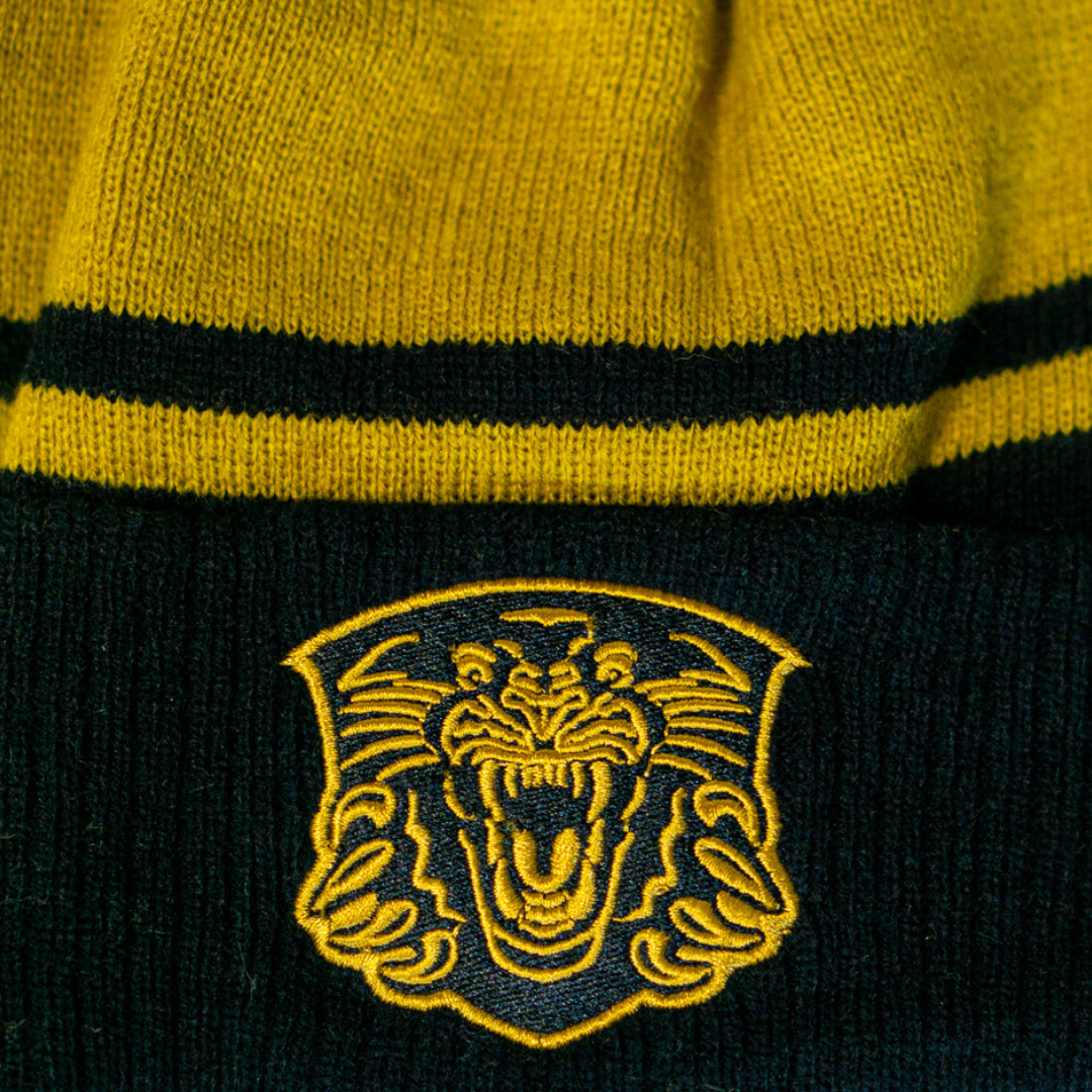 A close-up of the Nottingham Panthers 25-26 Gold Stripe Pom Knit by Panthersland, showing a bold embroidered tiger head logo on yellow and black knit—a must-have winter essential for any Panthers fan.