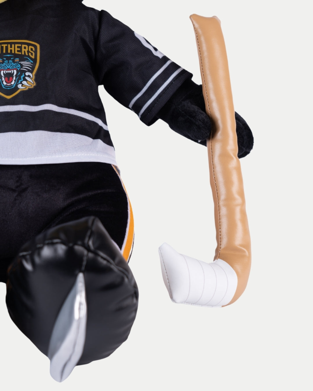 A close-up of the Big Ice Skating Paws Plush by Nottingham Panthers, wearing a black jersey with a partial team logo and holding a soft brown and white hockey stick, showing its left arm and leg.