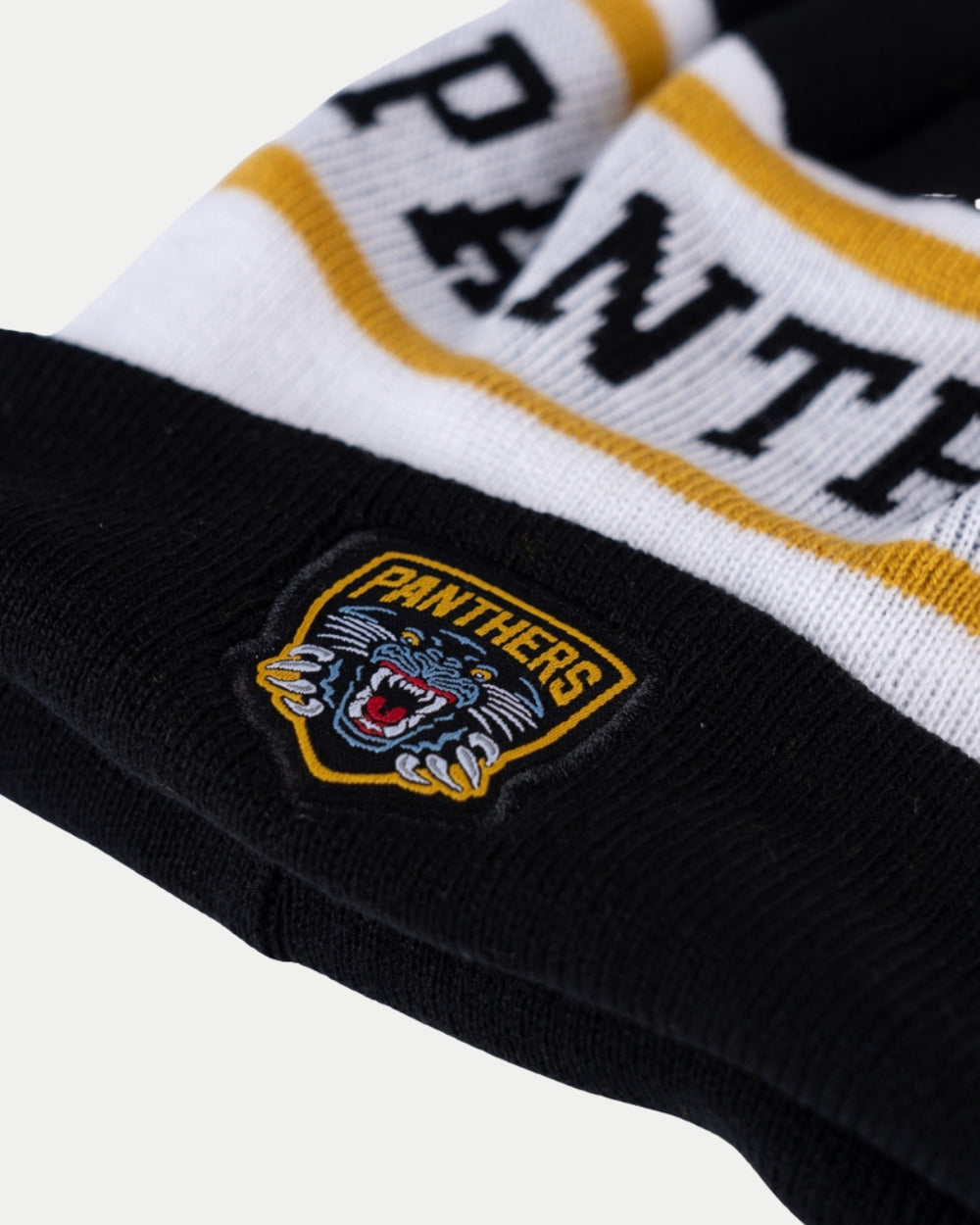Close-up of the Nottingham Panthers White Team Pom Knit by Nottingham Panthers, a black, white, and yellow hat with bold PANTHERS lettering and a stitched patch displaying the fierce panther logo with PANTHERS text.