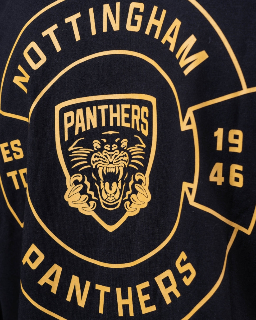 A close-up of The Nottingham Panthers Golden Logo Black Long Sleeve, featuring a yellow roaring panther logo inside a shield and Nottingham Panthers with 1946 accents on black fabric.