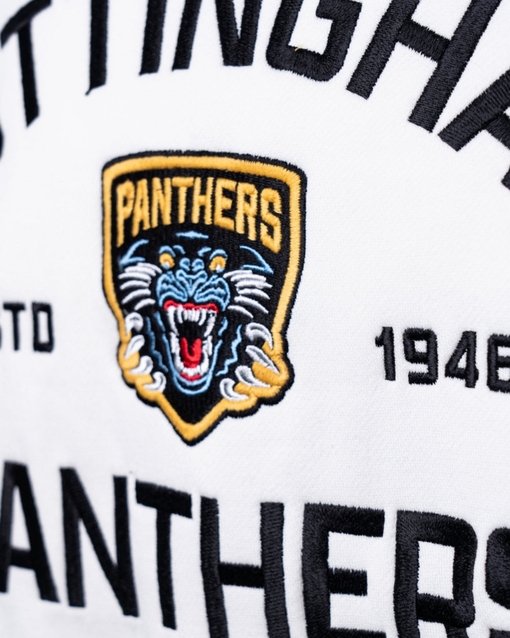 Close-up of the embroidered logo on The Nottingham Panthers Cream Logo Sweater, showing a snarling black panther head outlined in yellow, the word PANTHERS, and partial text with the year 1946 on white fabric.