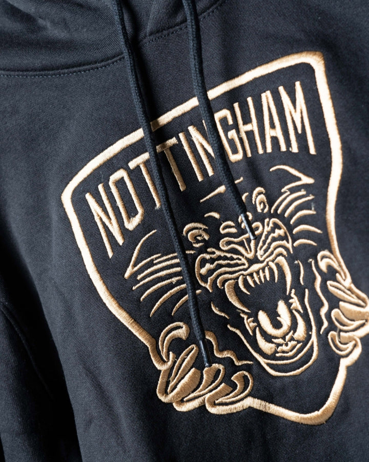 Close-up of The Nottingham Panthers Golden Twill Hockey Club Hoodie, showcasing an embroidered NOTTINGHAM logo above a stylized roaring panther face and claws outlined in beige thread.
