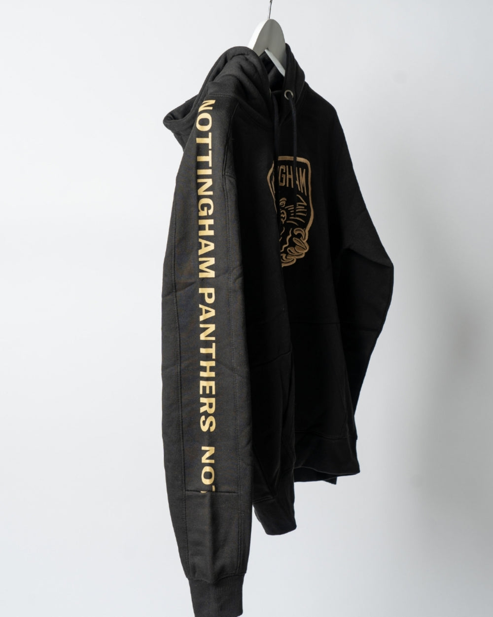 The Golden Twill Hockey Club Hoodie by The Nottingham Panthers hangs on a hanger, with NOTTINGHAM PANTHERS NO. in gold down the right sleeve and a bold gold logo on the chest. Displayed against a plain, light background.