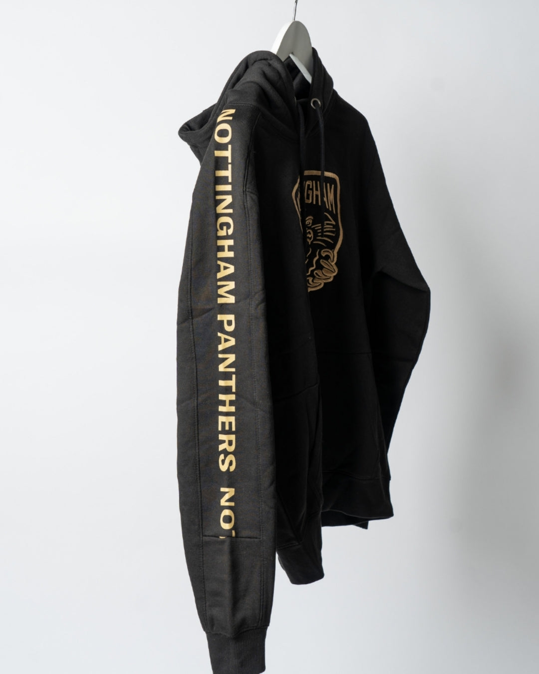 The Golden Twill Hockey Club Hoodie by The Nottingham Panthers hangs on a hanger, with NOTTINGHAM PANTHERS NO. in gold down the right sleeve and a bold gold logo on the chest. Displayed against a plain, light background.