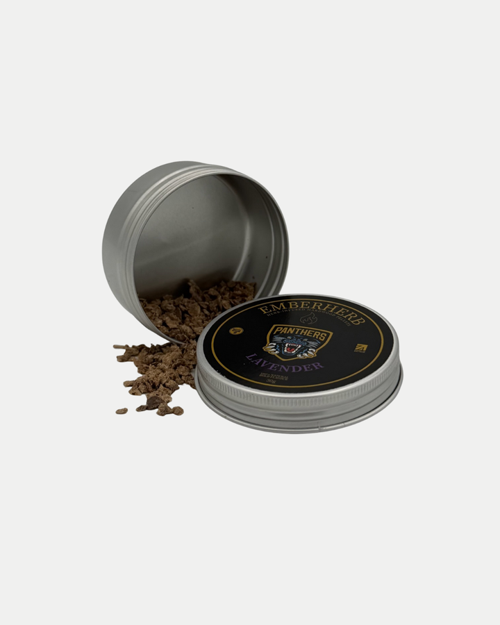 A round metal tin with a black and gold lid labeled Panthersland Nottingham Panthers Whiskey Smoker Kit lies open on its side, spilling brown dried plant pieces onto a white surface.