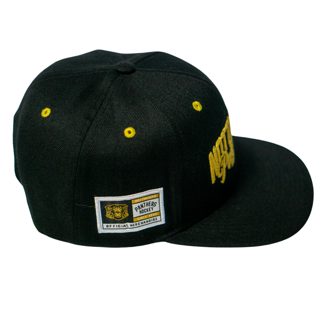 The Panthersland Nottingham Panthers 25-26 Script Snapback Cap is a black cap with gold embroidery, a Panthers Hockey Official Merchandise side patch, and yellow eyelets on the crown.