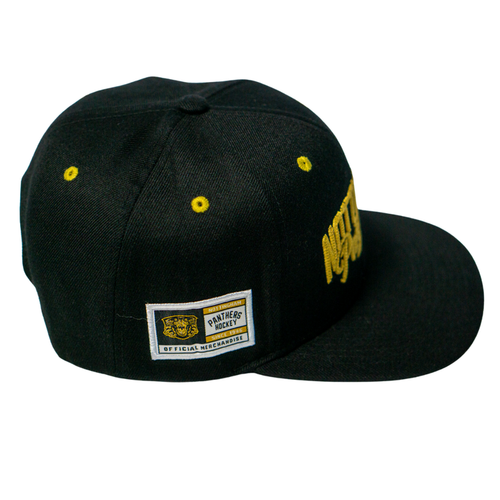 The Panthersland Nottingham Panthers 25-26 Script Snapback Cap is a black cap with gold embroidery, a Panthers Hockey Official Merchandise side patch, and yellow eyelets on the crown.