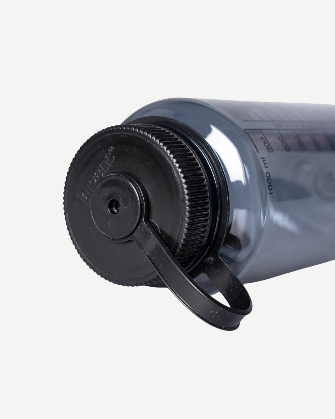 A close-up of the Panthers x Nalgene 1L Water Bottle by Panthersland, a gray BPA-free bottle with a black screw-on lid, attached carrying loop, measurement markings, and a wide mouth, lying on its side.