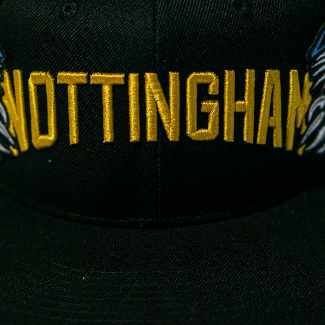 The Panthersland Nottingham Panthers 25-26 Big City Text Snapback Cap features bold yellow NOTTINGHAM embroidery, accented with blue and white wing details, making it a standout accessory for any fan.