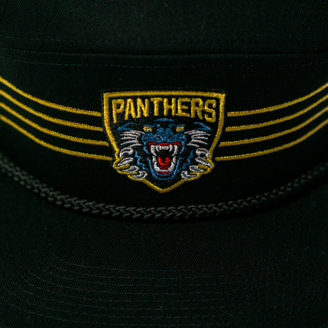 The Panthersland Nottingham Panthers 25-26 Four Stripe Flatbrim Cap is black with a yellow and blue embroidered crest showing a roaring panther and “PANTHERS” above it, plus bold gold stripes flanking the badge.