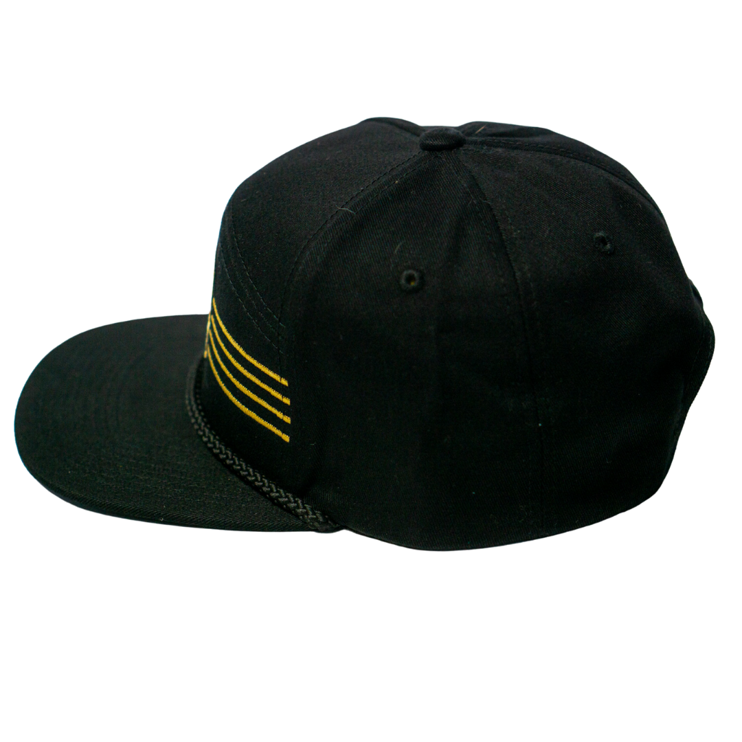 The Panthersland Nottingham Panthers 25-26 Four Stripe Flatbrim Cap is black with four yellow side stripes, gold stripe detail, ventilation eyelets, and a decorative black chain along the brim.