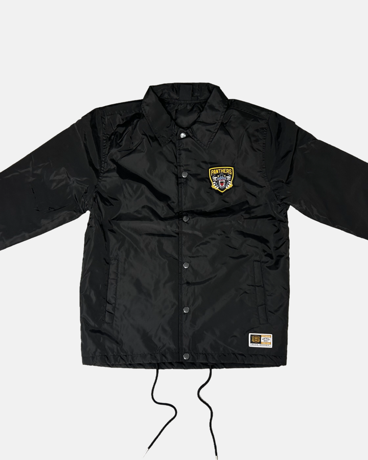 Introducing the Panthersland 26-27 Slice Coach Jacket—a black button-up coach jacket featuring a yellow Nottingham Panthers patch on the left chest and a small rectangular label near the bottom hem. This jacket includes front pockets, black drawstrings at the bottom, and classic coach jacket styling.