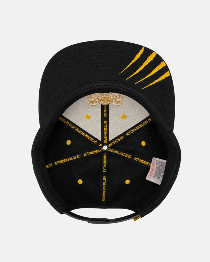 The Panthersland 26-27 Crest Snapback Cap is shown from underneath, highlighting gold embroidery, yellow stitching, NOTTINGHAM PANTHERS printed on the inner band, and three yellow claw mark designs on the underside of the brim—a sleek black snapback that showcases distinctive team pride and style.