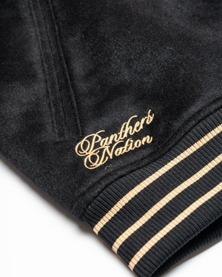 Close-up of the Panthersland Nottingham Panthers Varsity Jacket Black/Gold 25-26, featuring beige and black striped ribbed trim and Panthers Nation embroidered in gold script near the hem.