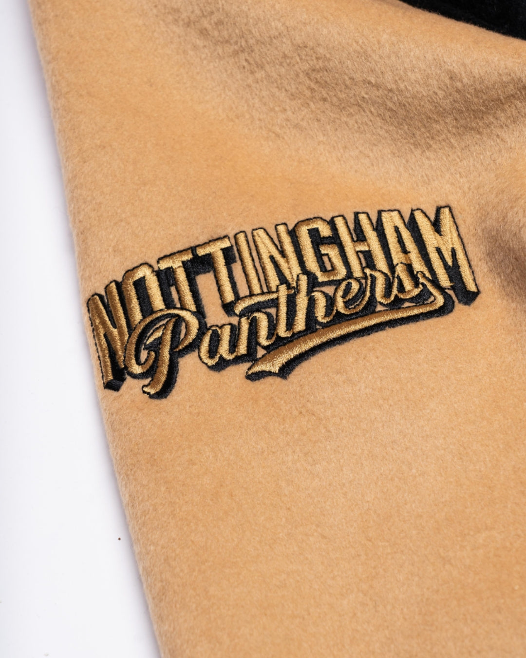 Close-up of tan fabric with Nottingham Panthers embroidered in gold and black, showcasing the Panthersland Nottingham Panthers Varsity Jacket Black/Gold 25-26—ideal for fans of the team.