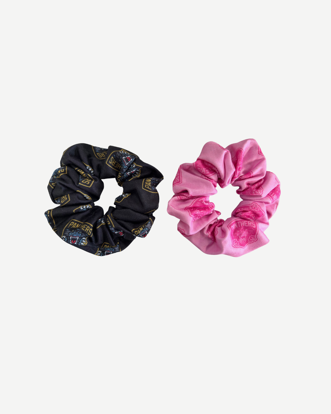 The Nottingham Panthers Hair Scrunchie Twin Pack by Panthersland features two scrunchies: one black with a multicolored pattern and one solid pink with an embossed design on a white background.