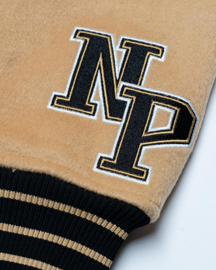 Close-up of the Nottingham Panthers Varsity Jacket Black/Gold 25-26 by Panthersland, showing tan fabric with black and gold varsity-style “N” and “P” embroidery beside a black ribbed cuff with tan stripes.