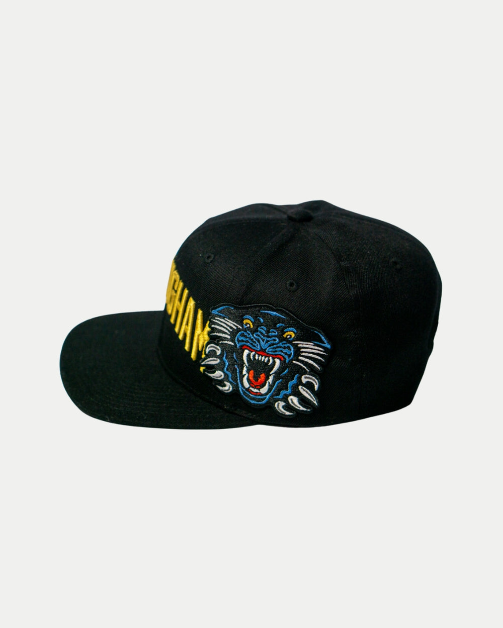 The Nottingham Panthers 25-26 Big City Text Snapback Cap by Panthersland features a bold black design with a colorful embroidered roaring blue panther on the front left panel and striking yellow text on the right side.
