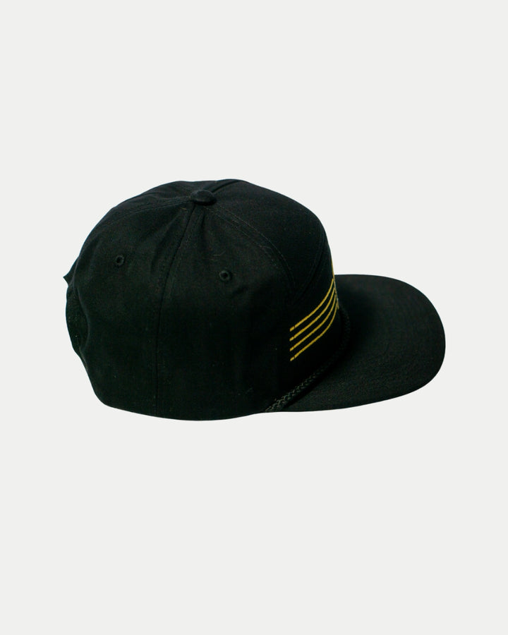 The Panthersland Nottingham Panthers 25-26 Four Stripe Flatbrim Cap features a sleek black design with four parallel gold stripes on the side, shown against a plain white background.