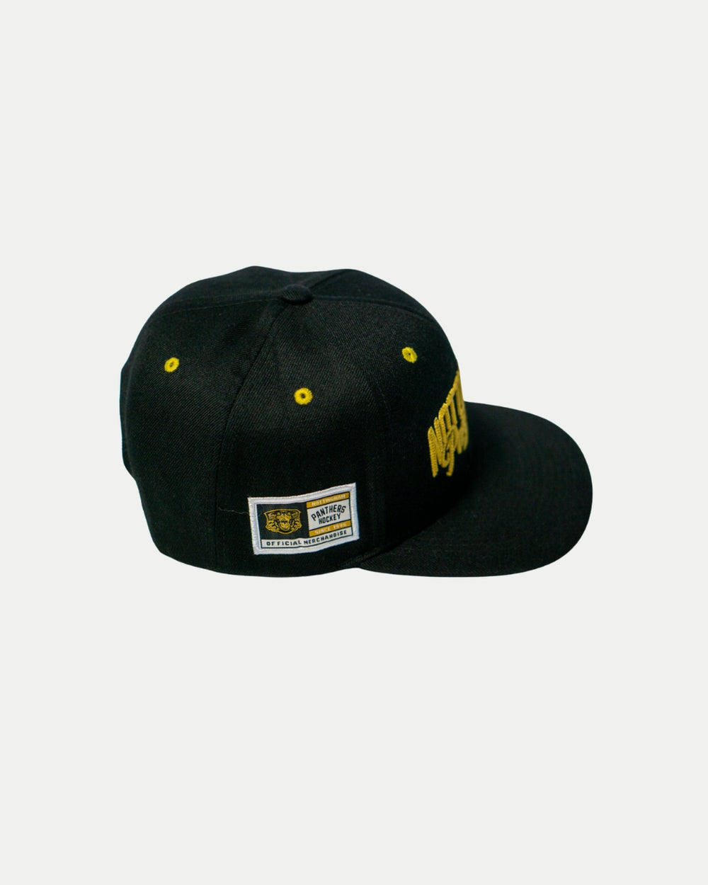 The Panthersland Nottingham Panthers 25-26 Script Snapback Cap features gold embroidery, yellow eyelets, and a front Nottingham Panthers script. A rectangular side patch with logo sits at an angle on the black cap against a white background.