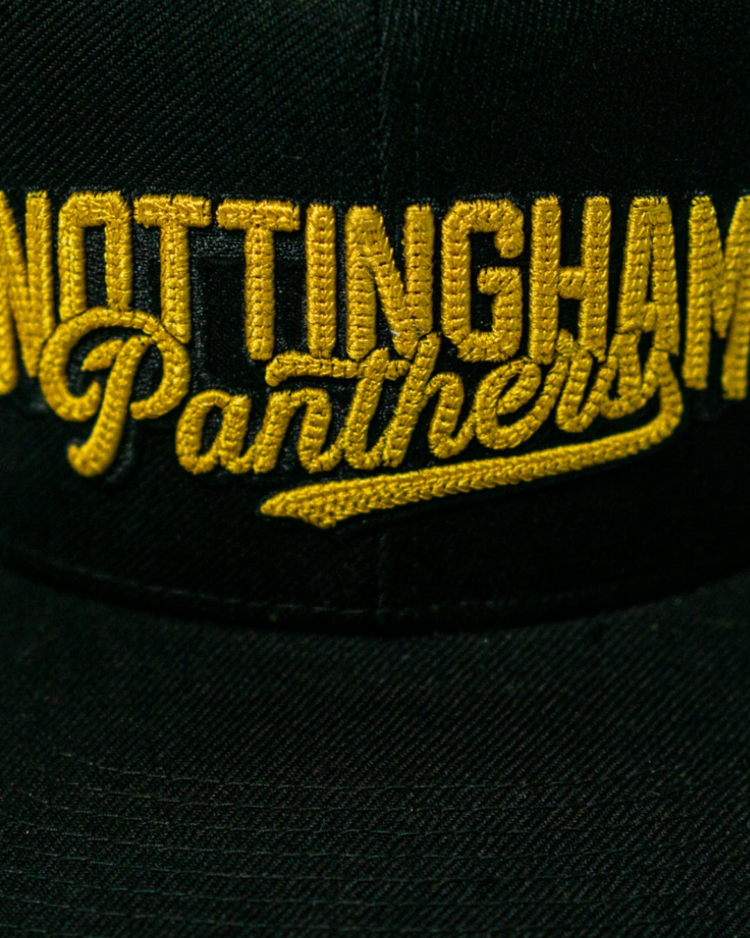 A close-up of the Panthersland Nottingham Panthers 25-26 Script Snapback Cap, a black hat with gold embroidery.