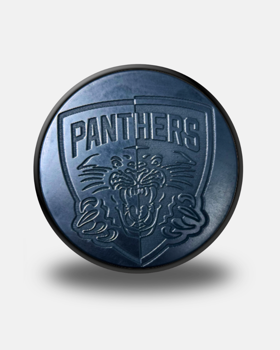A black Nottingham Panthers 26-27 Engraved Crest Puck from Panthersland, featuring an engraved panther logo with the word “PANTHERS” above it, casts a soft shadow on a white background.