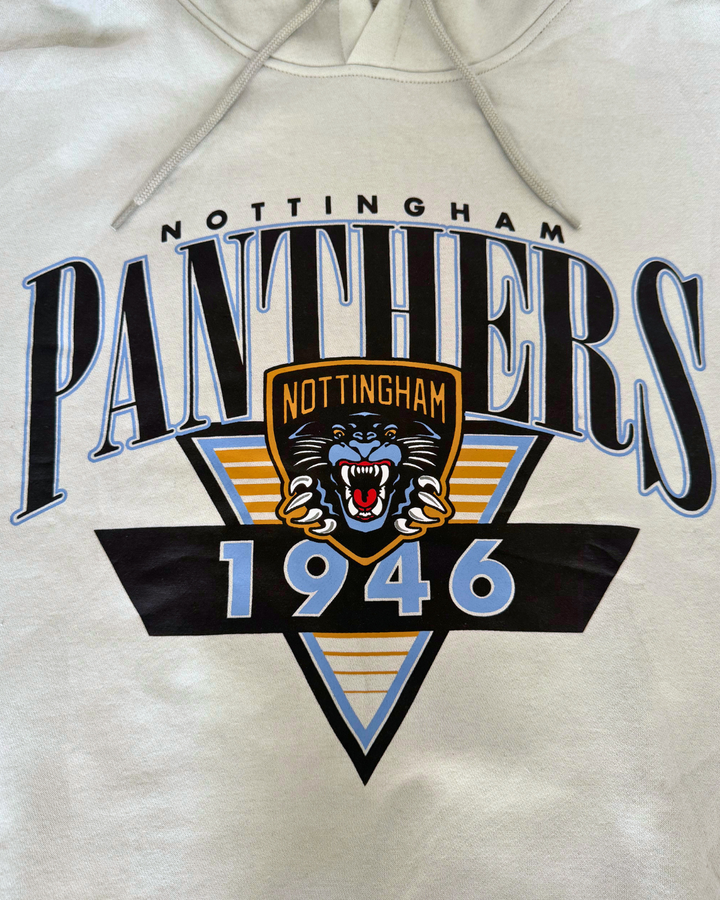 The Panthersland 26-27 Vintage Hoodie is a beige sweatshirt showcasing a retro Nottingham Panthers 1946 design, highlighted by a central roaring panther crest logo, bold blue and gold accents, and an eye-catching triangular background pattern.
